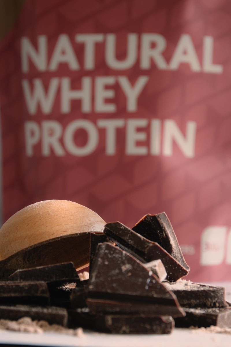 Chocolate pieces with a bag of Natural Whey Protein in the background